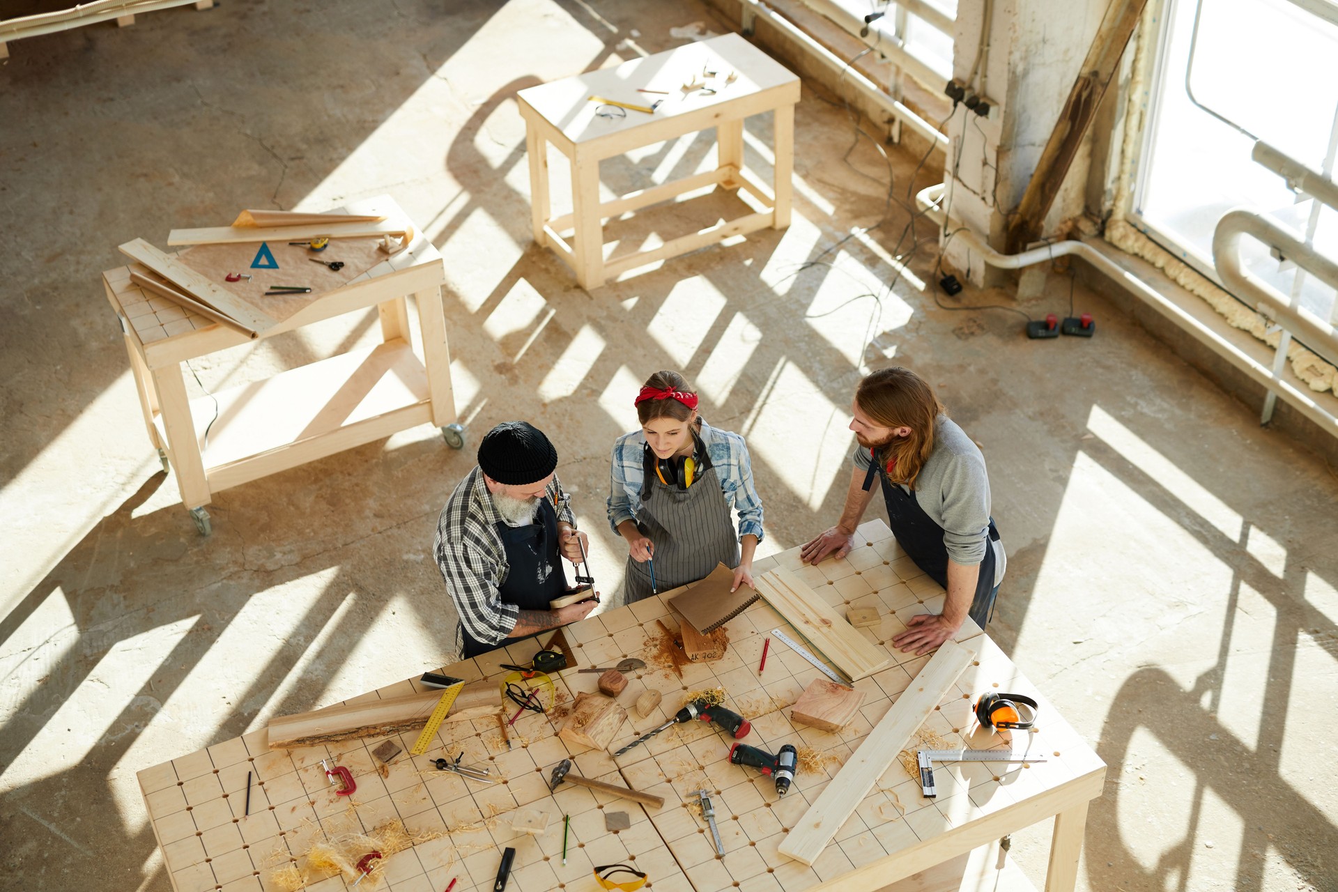 Vista de ángulo alto de trabajadores de carpintería ocupados usando pinza mientras examina los detalles de madera fabricados y haciendo notas en el Bloc de bocetos